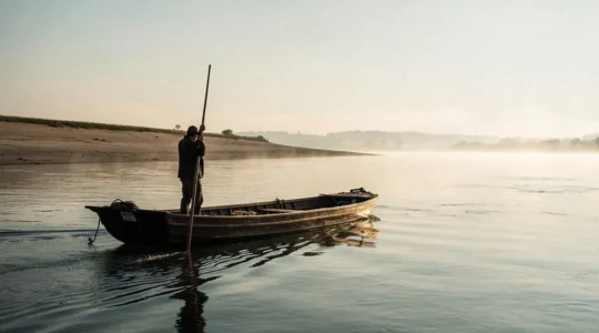 Marinier maniant une longue perche en bois à l'avant d'une toue cabanée traditionnelle sur les eaux calmes de la Loire au lever du jour